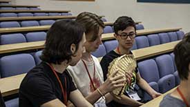 Three students sitting in lecture theatre, one holding an animal skeleton