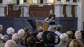 Speaker at Sheldonian Theatre, back view of audience in foreground