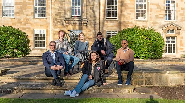 Six students sitting on steps outside Holywell Manor